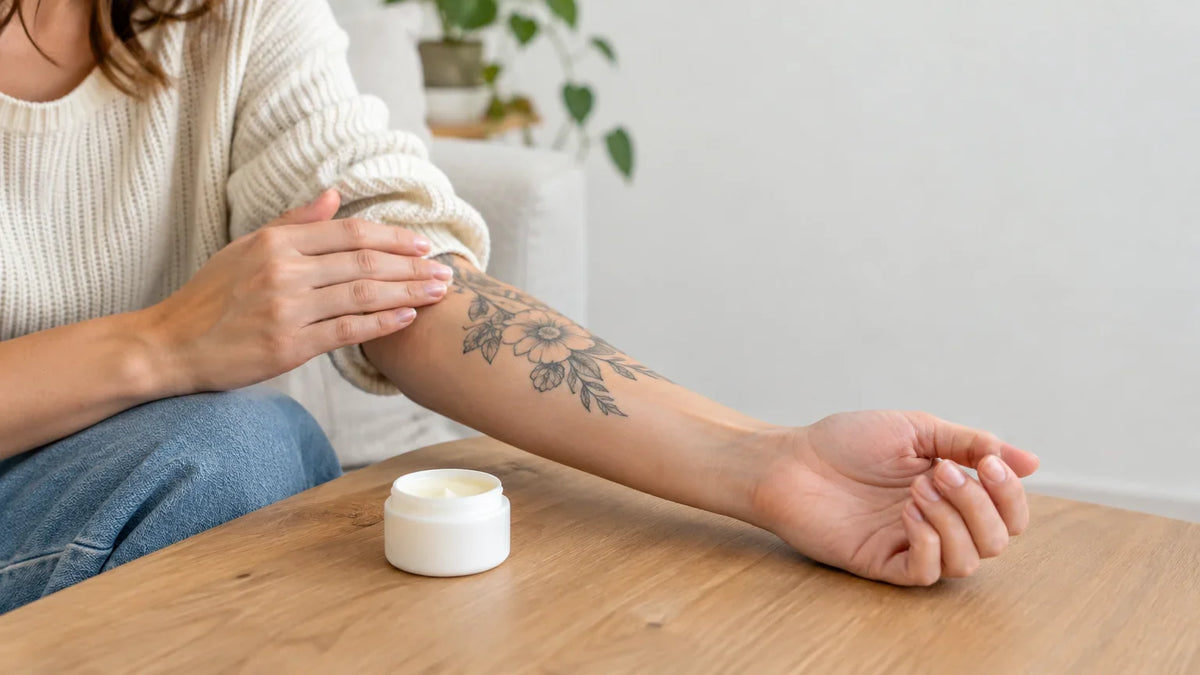 Avant-bras tatoué et pot de baume neutre posé sur une table, lumière naturelle Image