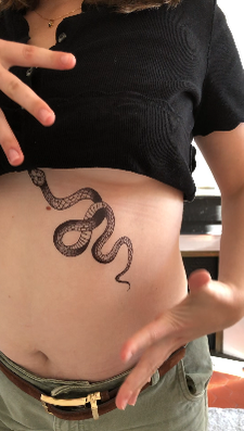Femme de 30ans qui applique le baume post-tatouage sur son ventre tatoué